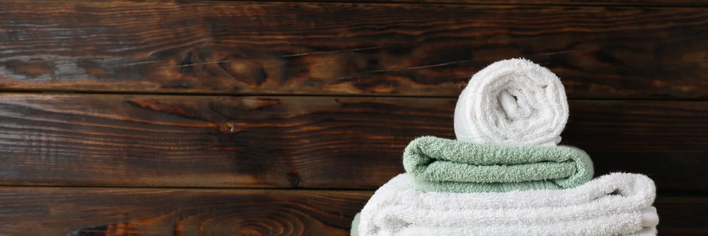 A rolled towel and a stack of folded towels on a wooden slat bench against dark timber.