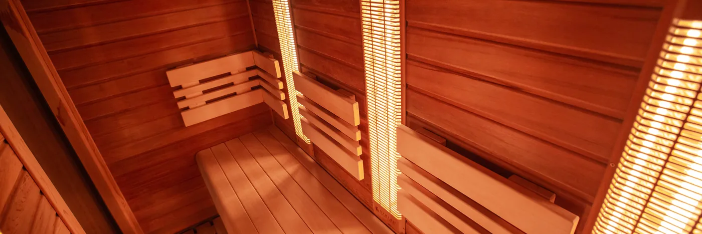The red-lit cedar interior of an infrared sauna, with heater panels glowing along the wall.